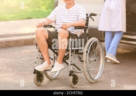 Arzt und junger Mann im Rollstuhl in der Nähe von van im Freien Stockfoto