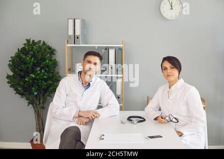 Frau und Mann Ärzte sitzen und Blick auf Kamera in Medizinische Klinik Stockfoto