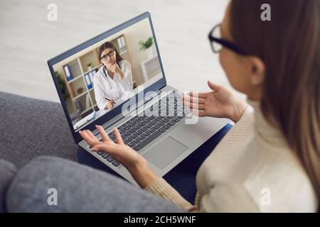 Arzt online. Weibliche Patientin erzählt Therapeut mit Laptop-Webcam zu Hause. Der Arzt konsultiert das Mädchen aus der Ferne. Stockfoto