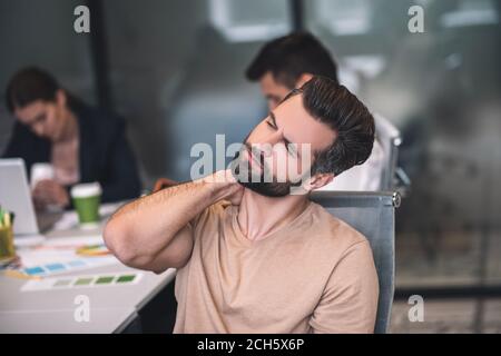 Bärtiger Mann, der beim Treffen sitzt und seinen Hals streckt Stockfoto