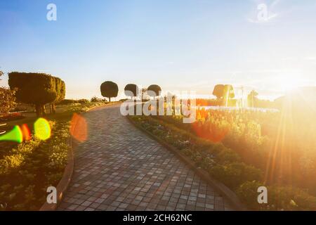 Ein ruhiger Blumengarten mit Springbrunnen auf dem Berg bei Sonnenuntergang, glühende Sonne untergeht hinter Blumengarten. Stockfoto