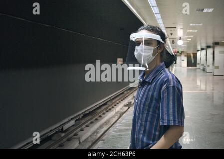 Isoliert langhaarige smart jungen Mann trägt Gesichtsschutz und Maske wartet darauf, dass die U-Bahn allein kommt Stockfoto