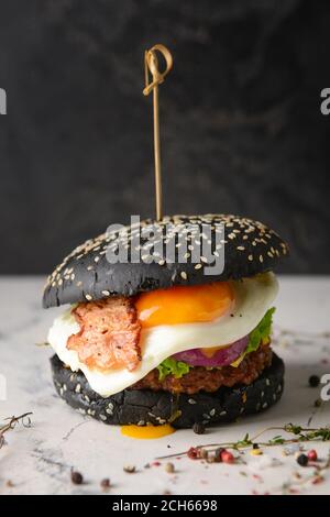 Leckerer Burger mit schwarzem Brötchen auf dem Tisch Stockfoto