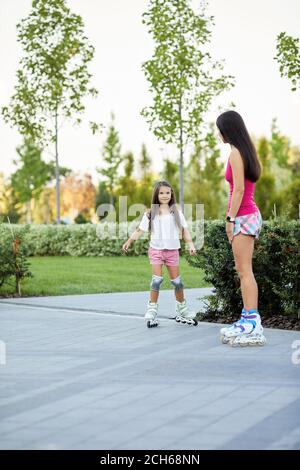 Junge Mutter und kleine Tochter Rollerskating im Park. Mädchen, die Spaß im Freien Stockfoto