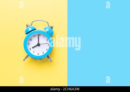 Blauer Wecker auf zweifarbigem gelben und blauen Hintergrund. Draufsicht, für Text platzieren - Bild Stockfoto