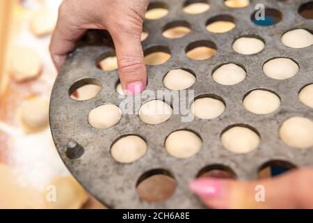 Frau quetscht rohe Knödel aus dem Gerät für die Herstellung Hausgemachte Knödel Stockfoto