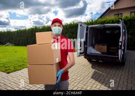 Lieferung Mann trägt medizinische Maske und Handschuhe Halten Karton Boxen. Lieferung Junge mit Schachteln in den Händen an der Lieferstelle Stockfoto