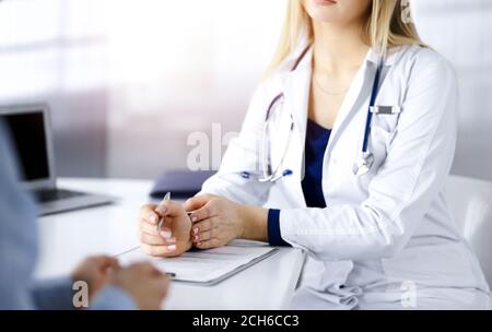 Unbekannte Ärztin verschreibt ihrem Patienten Antibiotika, während sie am Schreibtisch im sonnigen Kabinett in einer Klinik sitzen. Weiblich Stockfoto