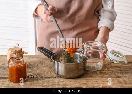 Frau Gießen leckere Pfirsichmarmelade aus Topf in Glas Küche Stockfoto