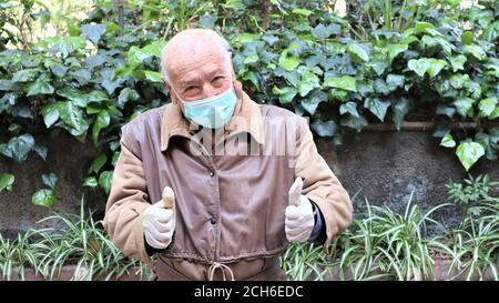 Alter Mann in medizinische Maske und Handschuhe Anti-Virus covid 19 älterer Mann zeigt Siegesgesten Stockfoto