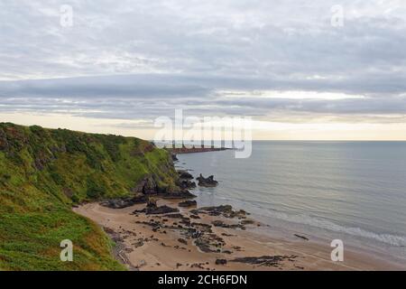 Der nördliche Rand des Sandstrandes im Naturschutzgebiet St. Cyrus mit seinen erodierten Klippen und Felsen in den Gewässern der Nordsee. Stockfoto