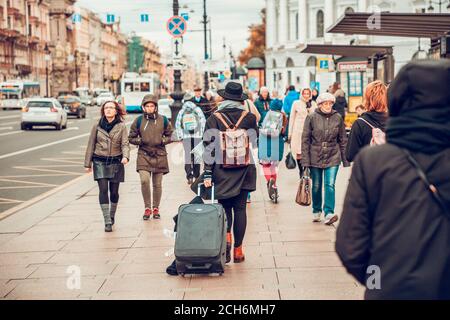 14.10.2018 Sankt Petersburg, Russland. Eine Frau geht die Straße entlang unter der Menge und rollt ihr Gepäck. Rückansicht. Reisen im Herbst. Stockfoto