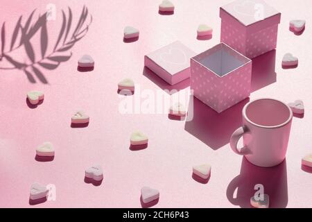Abstrakt Urlaub Hintergrund in rosa. Geometrisches Arrangement mit Geschenkschachteln, Zuckerherz-Süßigkeiten und Espresso-Kaffeetasse mit Schatten. Stockfoto