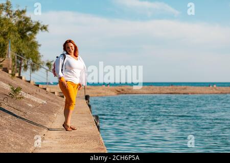 Der Sommer und die Feiertage. Eine glückliche übergewichtige Frau posiert auf einem Seebrücke. Speicherplatz kopieren. Stockfoto