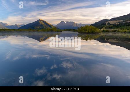 Foto des Mt Earnslaw aufgenommen in Glenorchy (NZ). Das Morgenlicht hebt langsam die Gipfel der Berge hervor, während der bewegungslose See wie ein Spiegel wirkt. Stockfoto