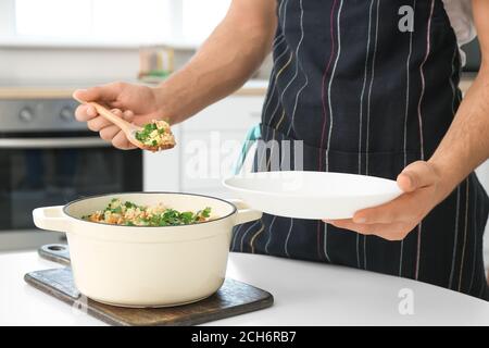 Junger Mann, der Reis mit Gemüse in der Küche auf den Teller legt, Nahaufnahme Stockfoto