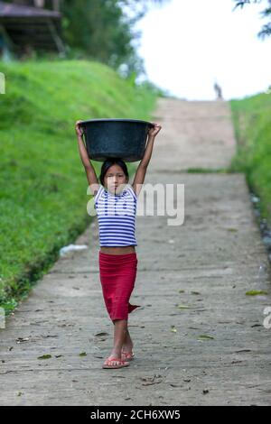 Ein junges peruanisches Mädchen, das einen Container mit Kleidung trägt, die zum Ufer der Stadt Indiana am Amazonas in Peru gewaschen werden soll. Stockfoto