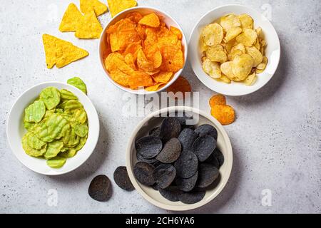 Verschiedene Arten von Kartoffelchips in weißen Schalen, grauer Hintergrund. Fast-Food-Konzept. Stockfoto