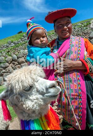 Eine Dame und ein Kind in bunten traditionellen peruanischen Kleidern, die ein Lama in den alten Ruinen von Sacsayhuaman in der Nähe von Cusco in Peru halten. Stockfoto