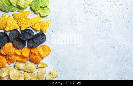 Verschiedene Arten von farbigen Kartoffelchips, grauer Hintergrund. Fast-Food-Konzept, ungesunde fetthaltige Kohlenhydrat-Lebensmittel. Stockfoto