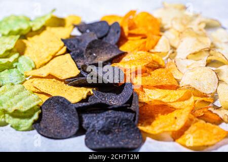 Verschiedene Arten von farbigen Kartoffelchips, grauer Hintergrund. Fast-Food-Konzept, ungesunde fetthaltige Kohlenhydrat-Lebensmittel. Stockfoto