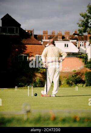 Ein Mann in traditionellen weißen gekleidet spielen Rasen Krocket halten Ein Krocketschläger neben einem Reifen im Sommer Tag in Großbritannien - Sommersport Stockfoto