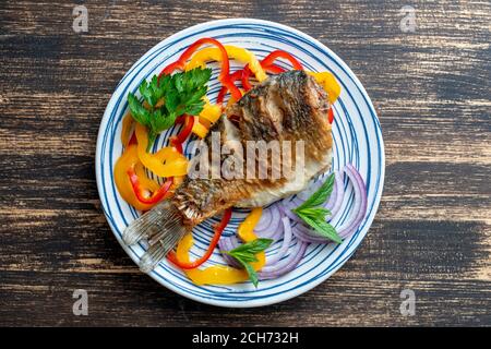 Gebratener Karausche mit Pfeffer und Zwiebel auf einem Teller auf Holzgrund. Draufsicht, Nahaufnahme Stockfoto