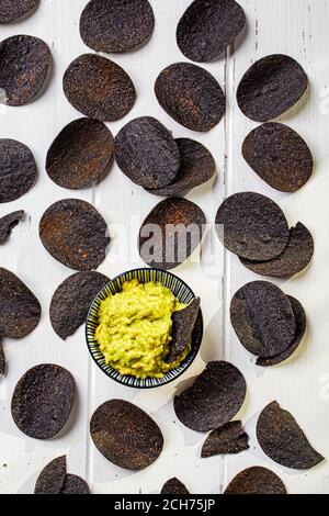 Schwarze Kartoffelchips mit Avocado Dip - Guacamole, weißer Hintergrund. Stockfoto