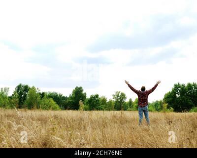 Ein Mann in einem herbstlichen Feld streckt seine Hände zum Himmel aus. Stockfoto