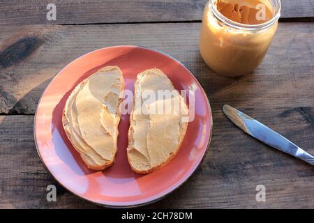 Erdnussbutter Toast auf Holzhintergrund. Brotscheibe mit Erdnusspaste auf einem Teller. Gesunder Snack für Kinder. Draufsicht Stockfoto