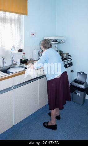 Neunzig Jahre alte Frau, die allein in ihrer Küche abspült. VEREINIGTES KÖNIGREICH Stockfoto