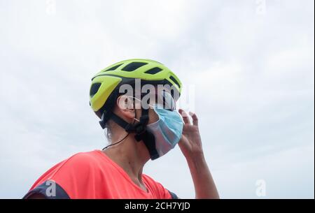Ältere Radfahrerin trägt Fahrradhelm, Sonnenbrille und Gesichtsmaske, Abdeckung. Stockfoto
