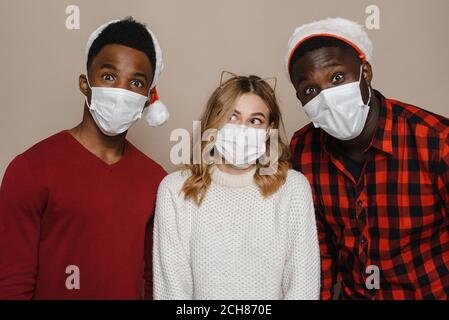 Drei junge Freunde tragen Weihnachtsmann Hüte und medizinische Masken. Bleiben Sie zu Hause und schützen Sie sich vor dem Coronavirus. Stockfoto