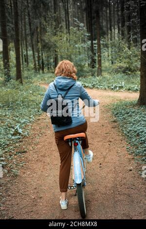 Eine Frau fährt auf einer Waldstraße in die Ferne Auf dem Fahrrad Stockfoto