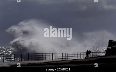 Spaziergänger beobachten riesige Wellen über die Küste in Whitley Bay, Tyne und Wear. Stockfoto