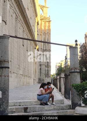 Sevilla, Spanien; 2. August 2020: Zwei junge Menschen mit Masken, die während der Corronavirus-Pandemie in Sevilla ihr Handy konsultieren Stockfoto