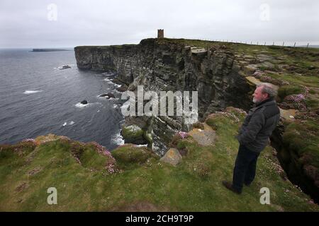 Die Besucher wandern auf den Klippen hoch über dem Meer bei Marwick Head in Orkney entlang, wo der Turm steht, der zur Erinnerung an Lord Kitchener gebaut wurde. Stockfoto