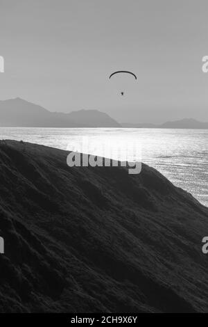 Person, die Paragliding auf den Klippen der Küste praktiziert. Schwarzweiß-Foto. Stockfoto