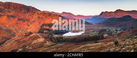 Kalter Wintersonnenaufgang hoch oben auf der Bergseite mit Blick ins Tal zur Spiegelreflexion auf Blea Tarn in Little Langdale. Stockfoto