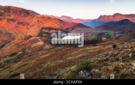 Kalter Wintersonnenaufgang hoch oben auf der Bergseite mit Blick ins Tal zur Spiegelreflexion auf Blea Tarn in Little Langdale. Stockfoto