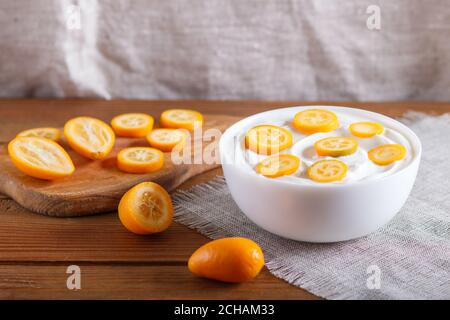 griechischer Joghurt mit Kumquat-Stücken in einem weißen Teller auf braunem Holzhintergrund, Nahaufnahme. Stockfoto