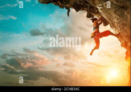 Athletische Frau klettert auf überhängenden Felsen mit Sonnenuntergang Himmel Hintergrund Stockfoto