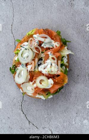 Ein halber Bagel mit Frischkäse, Lachs, frischen Kräutern und Gemüse auf einer Marmortheke Stockfoto