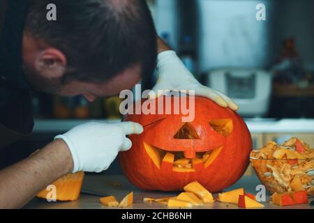 Mann macht Halloween Kürbis Kopf Jack Laterne auf Holztisch zu Hause, Nahaufnahme. Stockfoto
