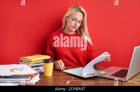 Junge Sekretärin Frau ist am Arbeitsplatz gelangweilt, blonde Frau sitzen am Tisch mit Papieren, Laptop. Isoliert auf rotem Hintergrund Stockfoto