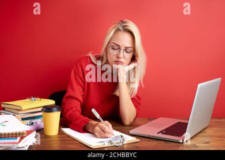 Schläfrig blonde verwirrt kaukasischen Frau Angestellter im Büro sitzen Arbeit am Schreibtisch, sie hat keine Energie zu arbeiten, isoliert roten Hintergrund Stockfoto