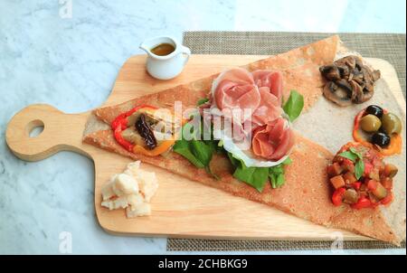 Vorspeise Crepe oder Crepe Antipasto mit Aufschnitt und Vielfalt Von sautenem Gemüse serviert auf hölzernen Brotbrett Stockfoto