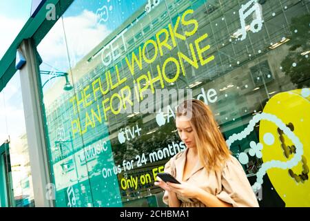 London - September 2020: Eine junge Frau auf einem Smartphone außerhalb eines EE-Handy-Shops Stockfoto