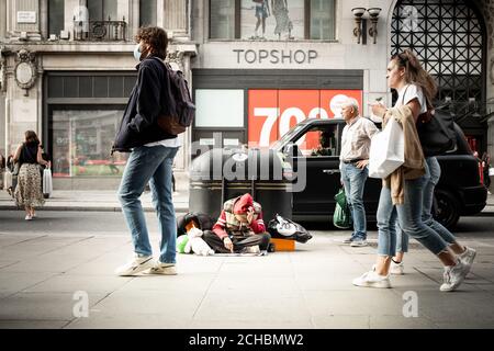 London - September 2020: Ein Obdachloser sitzt versumpt, während die Käufer an der Oxford Street vorbei laufen Stockfoto