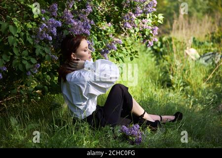 Schönes Mädchen im Frühjahr in den Zweigen der blühenden Flieder Büsche Porträt einer Frau an einem hellen Sommertag Stockfoto